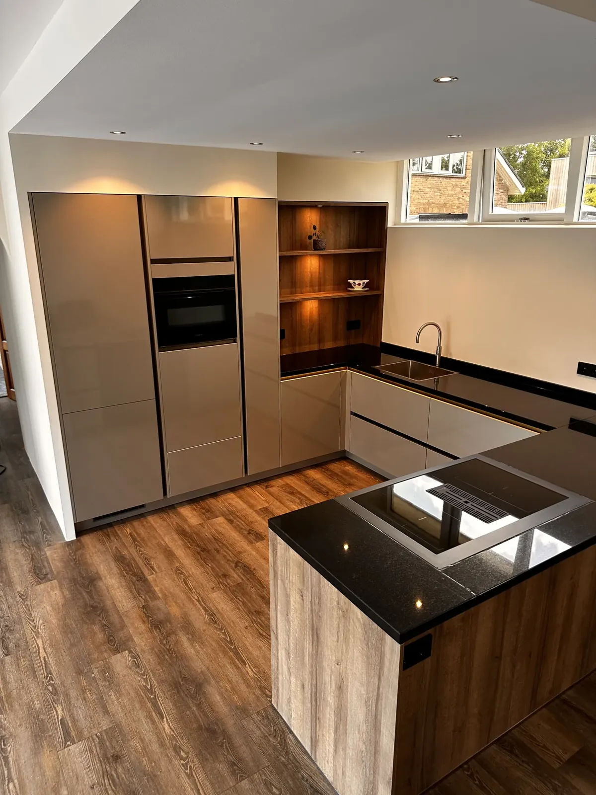 Keuken op maat Boskoop: hoekopstelling met kookeiland, taupe hoogglans kasten en houten nissen